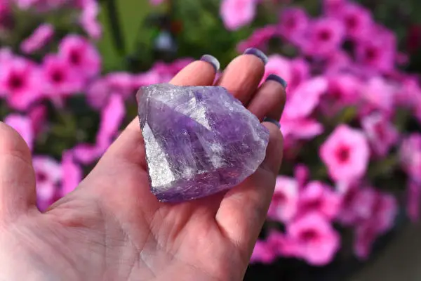 A close up image of a hand holding a large purple amethyst crystal-