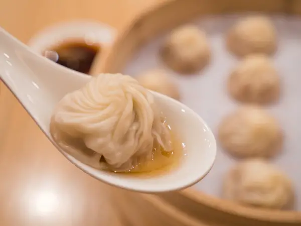 Closeup of Xiao Long Bao with soup in the spoon, Streamed Pork Dumplings