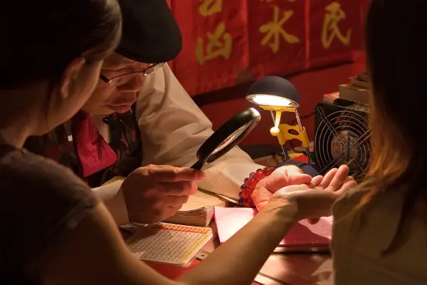 Elderly fortune-teller on a big city street, examining a hand of a client