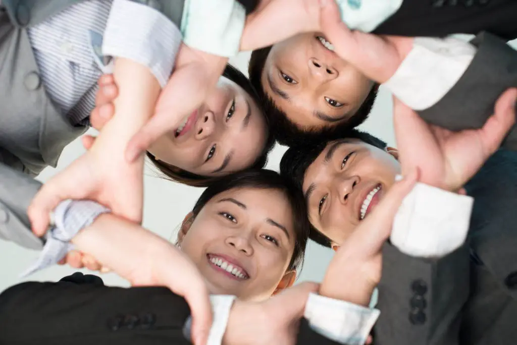 Chinese young business people holding hands and smiling at camera, view from below