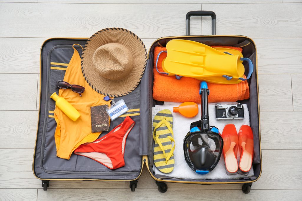 Suitcase with female beach accessories, immune certificate and snorkeling mask on white wooden background