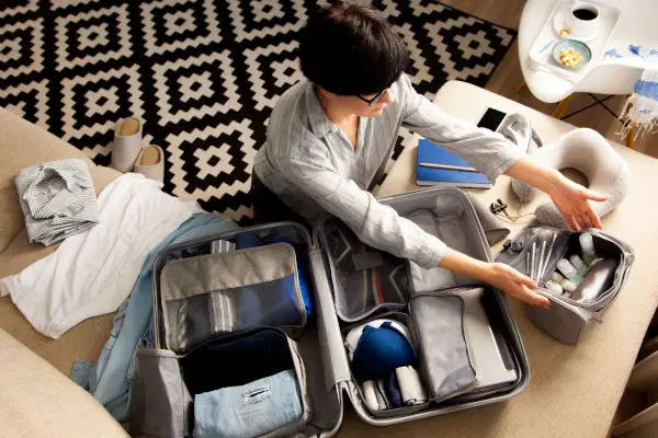 Female hands packing traveler case on bed, closeup. Beach accessories in opened suitcase. Travelling wheeled bag, different clothes.