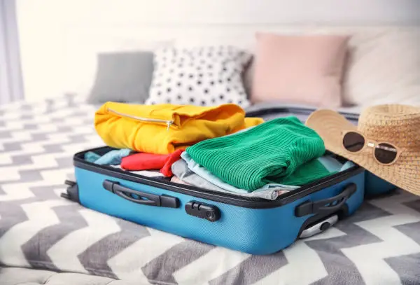 Open suitcase with different personal stuff on bed