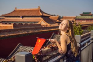 Enjoying vacation in China. Young woman with national chinese flag in Forbidden City. Travel to China concept.