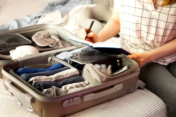 Female hands packing traveler case on bed, closeup. Beach accessories in opened suitcase. Travelling wheeled bag, different clothes.